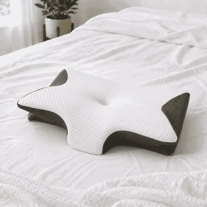 Butterfly-shaped sleep pillow with a white quilted top and charcoal mesh sides resting on a bed.